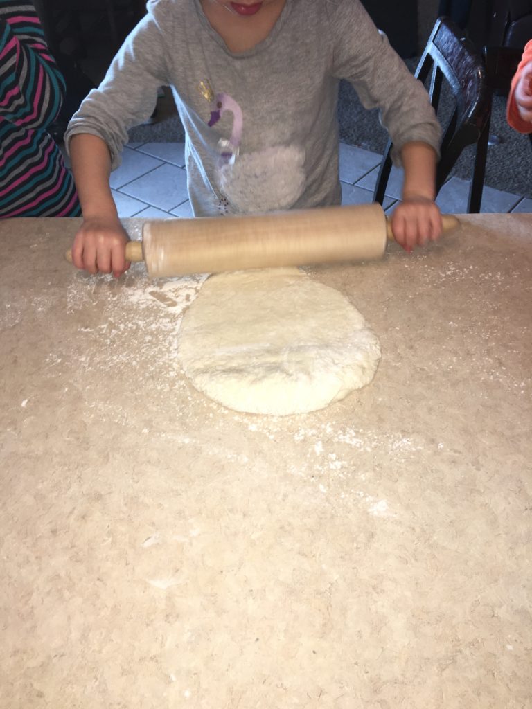 child rolling out some homemade pizza dough
