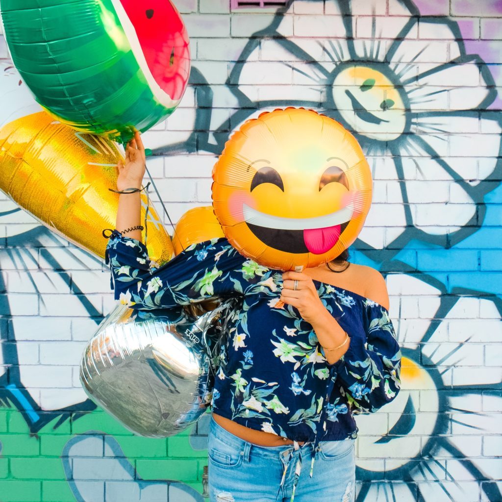 Woman holding a silly faced balloon in front of her face enjoying daily life
